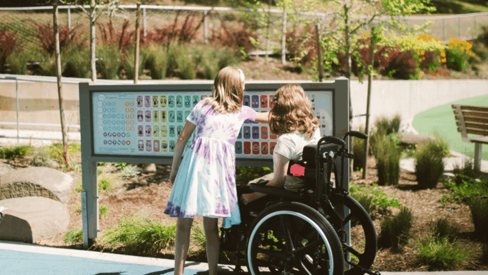 Une petite fille valide et une petite fille en fauteuil roulant regardant un panneau d'affichage - illustration de la formation Tourisme & Handicap